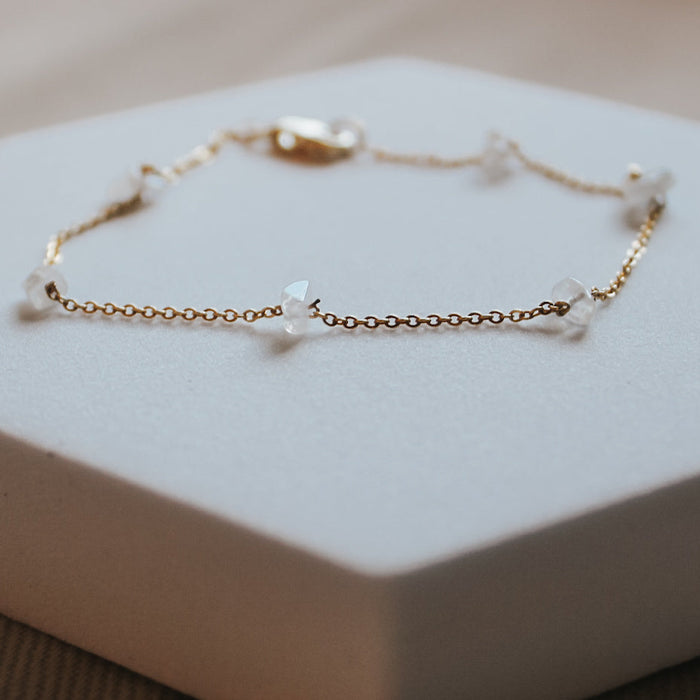 Gold bracelet with clear stones on a white hexagonal stand